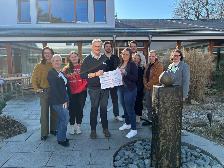 Mitarbeitende der VW Group Norderstedt überreichen symbolisch einen Spendenscheck an Einrichtungsleiter Jens Klindworth und andere Mitarbeitende aus dem Albertinen Hospiz Norderstedt für die Hospizarbeit im Hospizgarten vor dem Hospiz.