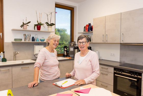 Zwei ehrenamtliche Mitarbeiterinnen schauen in der Küche des Albertinen Hospiz Norderstedt in die Kamera