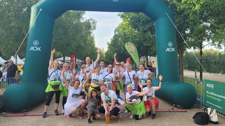 Mitarbeitende aus Pflege, Koordination/Verwaltung, Ehrenamt und Geschäftsführung des Albertinen Hospiz Norderstedt beim AOK-Firmenlauf Norderstedt 2026 blicken gemeinsam im Zieleinlauf ausgelassen und glücklick in die Kamera. Mitarbeitende aus Pflege, Koordination/Verwaltung, Ehrenamt und Geschäftsführung des Albertinen Hospiz Norderstedt beim AOK-Firmenlauf Norderstedt 2026 blicken gemeinsam im Zieleinlauf ausgelassen und glücklick in die Kamera.