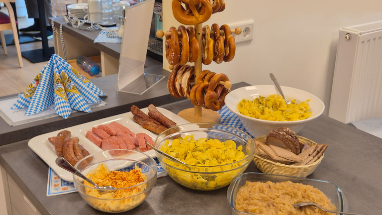 Oktoberfestlich dekoriertes Buffet mit Brezeln, Bratwurst, Leberkäse, Kartoffelsalat, Sauerkraut und Brot im Albertinen Hospiz Norderstedt.