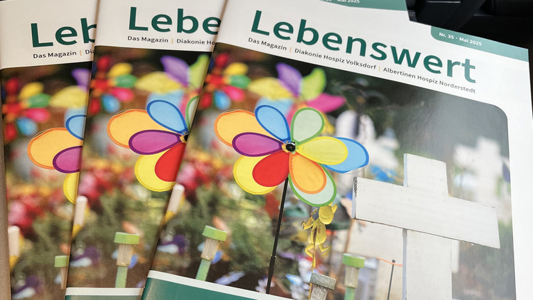 Lebenswert Magazin gestapelt auf Schoß, neue Ausgabe Lebenswert, gemeinsame Zeitschrift Diakonie Hospiz Volksdorf und Albertinen Hospiz Norderstedt