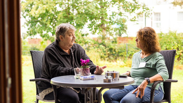 Eine ehrenamtliche Mitarbeiterin sitzt mit Hospizgast auf der Terrasse im Albertinen Hospiz Norderstedt